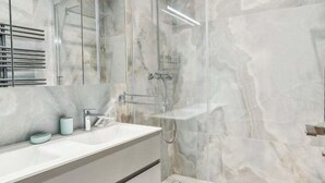 Une salle de bain moderne avec une douche en verre, un grand miroir et un mur recouvert de carreaux de marbre.