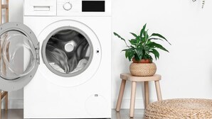 A front-loading washing machine in a clean, modern laundry room with a small wooden stool and a potted plant. - 106-Suite Cece - Superb Duplex in Paris (Paris)