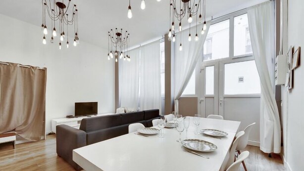 A modern living room with a dining area, large windows, and a chandelier. - 106-Suite Cece - Superb Duplex in Paris (Paris)