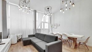 A modern living room with a grey sectional sofa, a dining area with a white table and chairs, and a chandelier with multiple light bulbs. - 106-Suite Cece - Superb Duplex in Paris (Paris)