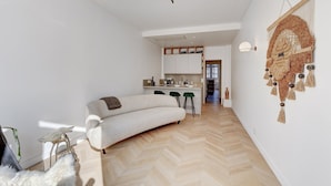 A modern living room with a sofa, a small kitchen area, and a decorative wall hanging. - 633 Suite Victoria - Superb apartment in Paris (Paris 02 Bourse)