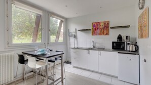 A modern kitchen with white cabinets, a dining table with chairs, a window, and a colorful painting on the wall. - 235 Home Madrid Concept (Paris 15 Vaugirard)
