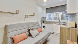 A compact living space with a grey sofa, a washing machine, and a kitchenette. - 143 Suite La Française Superb Apartment in Paris (Paris 19 Buttes-Chaumont)