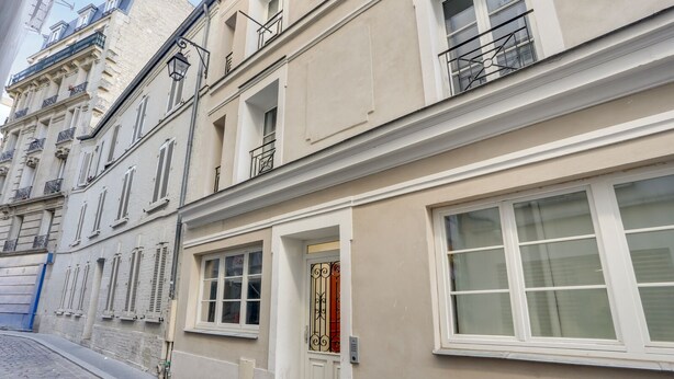 A row of buildings with white facades and multiple windows, featuring a mix of balconies and ground-level entrances. - 143 Suite La Française Superb Apartment in Paris (Paris 19 Buttes-Chaumont)