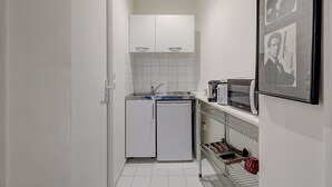 Cocina compacta con armarios blancos, un lavamanos, estufa y microondas. Hay un estante pequeño con un tostador y una taza roja.