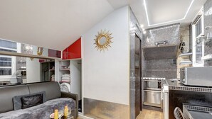 Un espace de vie compact comprenant un canapé, une petite table avec des boissons, une kitchenette et une salle de bain avec douche.