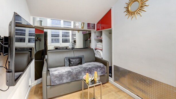 Un espace de vie compact comprenant un canapé, une petite table avec des verres et une armoire aux portes rouges.