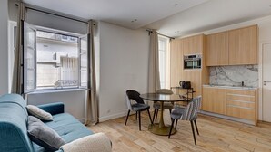 Ein kompakter Wohnbereich mit einer Couch, einem Esstisch, Stühlen und einer Küchenzeile mit Holzschränken und einer Marmor-Spritzschutzwand.