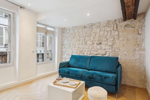 Un salon avec un canapé de couleur turquoise, une table basse blanche et un mur en pierre.