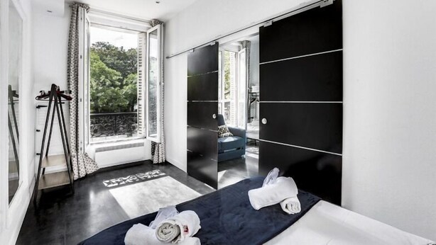 Ein modernes Hotelzimmer mit einem großen Bett, einem Kleiderschrank und einem Balkon mit Blick auf Grünflächen.