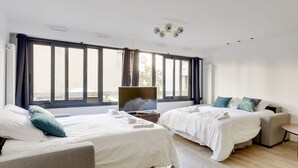 A modern hotel room with two beds, a TV, and large windows. - 173 Suite Eiffel - Superb apartment in Paris. (Paris 15 Vaugirard)