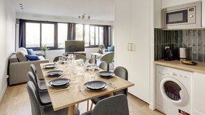 A modern kitchen with a microwave, washing machine, and a dining area set up with a table, chairs, and a TV. - 173 Suite Eiffel - Superb apartment in Paris. (Paris 15 Vaugirard)