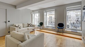 A modern living room with a sofa set, a small table, and two chairs. There are large windows with decorative iron railings. - 169 Suite W - Elegant Apartment in Paris (Paris 02 Bourse)