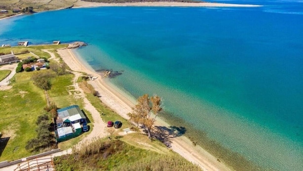 Luchtbeeld van een kustbezit met een strand, een omheind gebied met geparkeerde auto's en een gebouw met een groen dak.