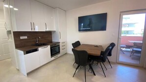 Een moderne keuken met witte kasten, een houten aanrecht en een ingebouwde oven. Er staat een eettafel met zwarte stoelen en een televisie is aan de muur bevestigd.