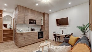 A modern kitchen with wooden cabinets, a microwave, and an oven. There is a dining area with a table and chairs, and a sofa with cushions.