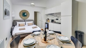 A modern hotel room with a bed, a dining table set for two, a kitchen area, and a large window. - 141 Suite Klein - Superb apartment in Paris. (Paris 03 Temple)