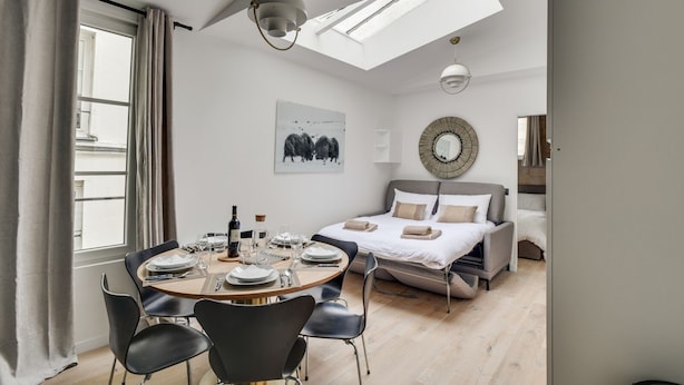 A modern bedroom with a skylight, a dining area with a round table, and a bed with a headboard. - 141 Suite Klein - Superb apartment in Paris. (Paris 03 Temple)