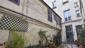 A courtyard with potted plants, a lattice fence, and a building with multiple windows and doors. - 141 Suite Klein - Superb apartment in Paris. (Paris 03 Temple)