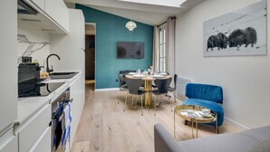 A modern kitchen with a dining area, a blue sofa, and a painting of bison. - 141 Suite Klein - Superb apartment in Paris. (Paris 03 Temple)