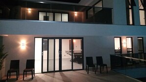 A modern two-story building with a glass balcony, sliding doors, and a pool area with chairs. - Queen Room with Pool View (Oistins)