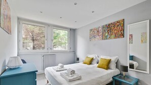 Ein modernes Schlafzimmer mit großem Fenster, einem Bett mit weißen Leinen, gelben Kissen und Bildern an den Wänden.