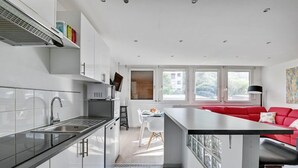 Eine moderne Küche mit weißen Schränken, einer Edelstahlspüle und einem Essbereich mit einem roten Sofa und einem weißen Tisch.