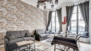 Un salón moderno con pared de ladrillo, un sofá, una mesa de centro y una zona de comedor con una mesa preparada para dos personas.