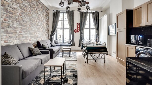 Una sala de estar moderna con un sofá gris, una mesa de comedor y una zona de cocina con lavadora.