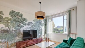 A modern living room with a large flat-screen TV, a green sofa, a white coffee table, and a wooden cabinet. - 628 Suite Foret - Superb apartment in Paris (Paris 14 Observatoire)