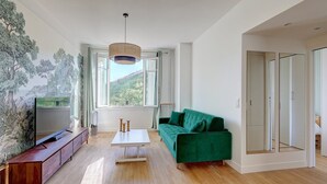 A modern living room with a green sofa, a flat-screen TV, and a large window with a view of a hill. - 628 Suite Foret - Superb apartment in Paris (Paris 14 Observatoire)