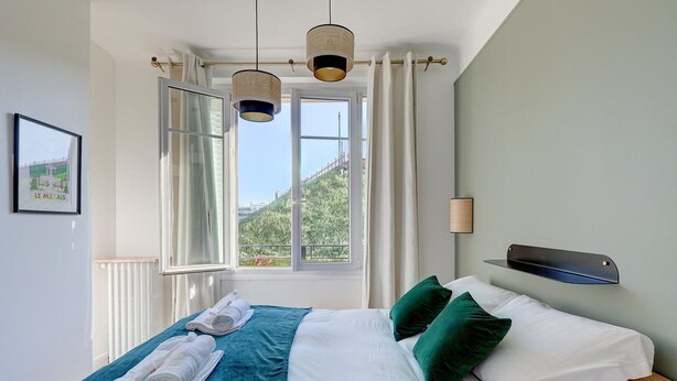 A hotel room with a bed, two pillows, a window with curtains, a radiator, and a wall-mounted shelf. - 628 Suite Foret - Superb apartment in Paris (Paris 14 Observatoire)