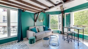 Ein Zimmer mit einer Couch, zwei kleinen Tischen, einem gemusterten Teppich und einem Balkon mit Geländer.