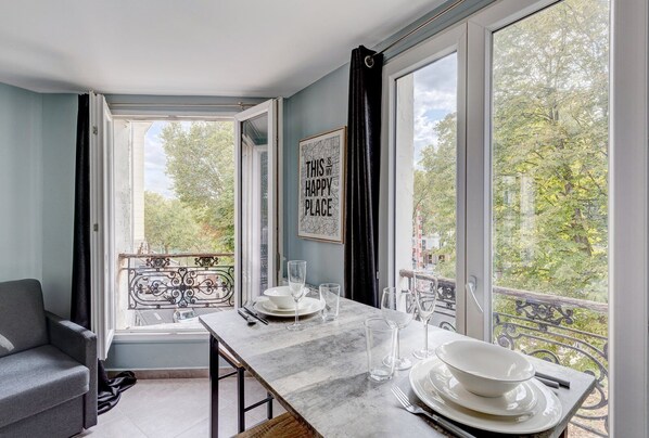 A dining area with a table set for four, a view of trees and buildings through large windows, and a framed quote on the wall.