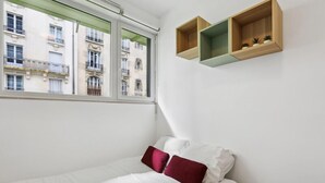 Ein Schlafzimmer mit einem Bett, zwei Kissen, einem Fenster und zwei Holzregalen mit Pflanzen.
