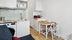 Eine kompakte Küche mit weißen Schränken, einer Waschmaschine, einer Kaffeemaschine und einem Essbereich mit Tisch und Stühlen.