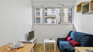 Ein kleines, modernes Wohnzimmer mit einer Couch, einem Fernseher und einem Essbereich mit Tisch und Stühlen.