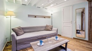 Una habitación moderna con un sofá de color gris claro, una mesa de centro de madera con dos tazas, una lámpara de pie y un espejo en la pared.