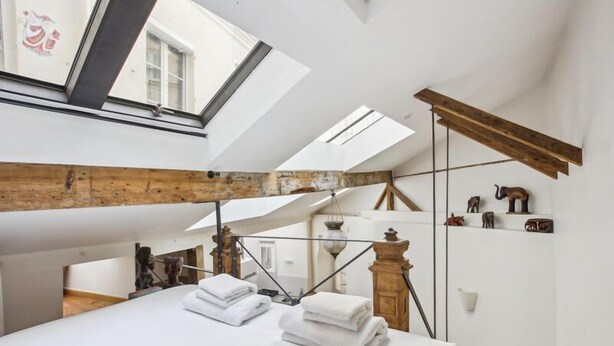 Un dormitorio con tragaluces, vigas de madera y una cama con toallas blancas ordenadas.