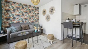 Un saló modern amb un sofà gris, una taula de centre rodona, i una zona de cuina amb un tamboret.