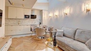 A modern living room with a herringbone floor, a grey sofa, a glass coffee table, and a dining area with a round table and chairs. - 348 Ponthieu - Superb apartment in Paris (Paris 08 Élysée)