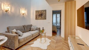 A modern living room with a sofa, a small round table, and a painting on the wall. - 348 Ponthieu - Superb apartment in Paris (Paris 08 Élysée)