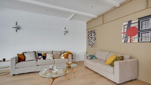 A modern living room with two sofas, a glass coffee table, and abstract wall art. - 178 Suite Cesar - Superb apartment in Paris (Paris 11 Popincourt)
