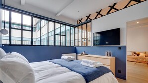 A modern hotel room with a large bed, a bedside table, a TV, and a view of the city through large windows. - 178 Suite Cesar - Superb apartment in Paris (Paris 11 Popincourt)