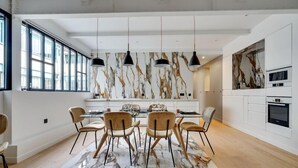A modern kitchen with a marble backsplash, pendant lights, and a dining area with a marble table and chairs. - 178 Suite Cesar - Superb apartment in Paris (Paris 11 Popincourt)