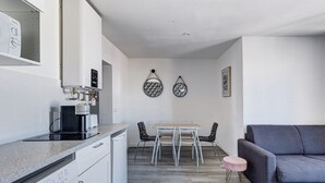 A compact kitchen with a washing machine, a coffee maker, and a dining area with a table and chairs. - 803 Suite Parisian - Superb apartment (Bagnolet)