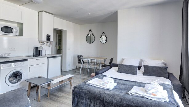 A compact hotel room with a kitchenette, a bed with grey bedding, a washing machine, and a dining area with a table and chairs. - 803 Suite Parisian - Superb apartment (Bagnolet)