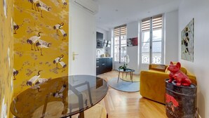 A modern living space with a dining area, kitchen, and a yellow wall with a crane pattern. - 210 Suite Chanel - Superb apartment in Paris (Paris 04 Hôtel-de-Ville)