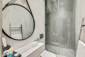 A modern bathroom with a large mirror, a glass-enclosed shower, and a white marble sink. - 210 Suite Chanel - Superb apartment in Paris (Paris 04 Hôtel-de-Ville)