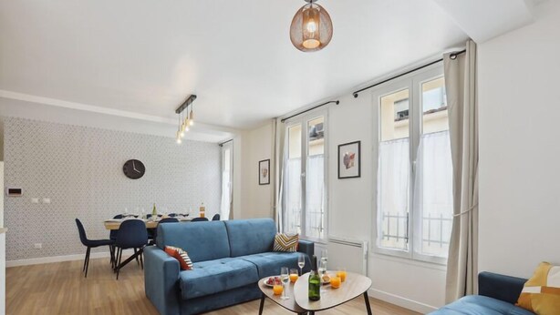 A modern living room with a blue sofa, a dining area with a table and chairs, and large windows with curtains. - 865 Suite Jasmin - Superb apartment (Montreuil)
